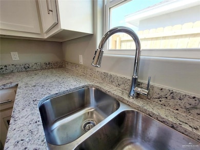 Kitchen view of a sink, light stone countertops, and white cabinets