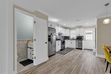 Kitchen with appliances with stainless steel finishes, hanging light fixtures, backsplash, ornamental molding, and white cabinets