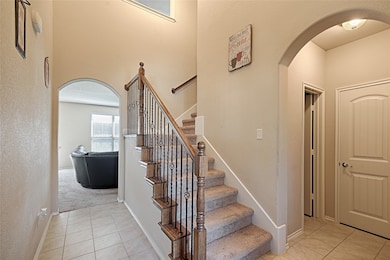Staircase with arched walkways, tile patterned flooring, a high ceiling, and a textured wall
