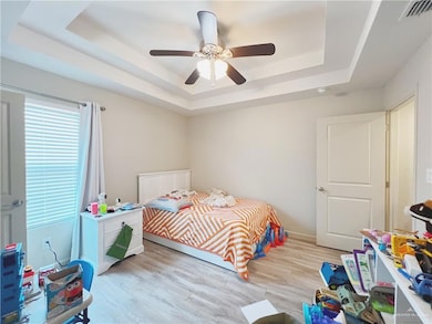Bedroom featuring a raised ceiling, light wood-type flooring, and a ceiling fan