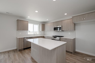 Kitchen with light brown cabinetry, decorative backsplash, stainless steel appliances, light stone countertops, and modern cabinets