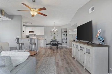 Living room with light wood-style floors, a ceiling fan, a textured ceiling, a chandelier, and baseboards