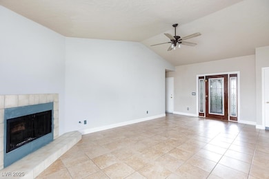 Unfurnished living room featuring a tile fireplace, lofted ceiling, light tile patterned floors, and a ceiling fan