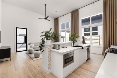 Kitchen with light wood-type flooring, white cabinetry, a high ceiling, light stone countertops, and appliances with stainless steel finishes