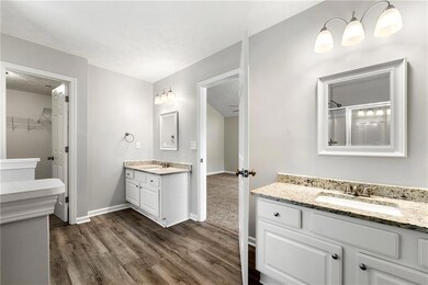 Bathroom with wood finished floors, two vanities, a walk in closet, a textured ceiling, and a shower