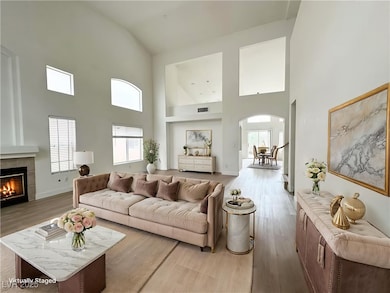 Living area featuring light wood-type flooring, a tiled fireplace, high vaulted ceiling, and arched walkways