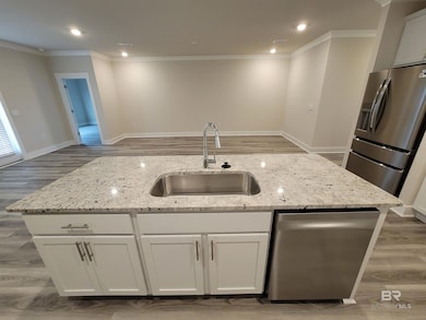Kitchen featuring light wood finished floors, a center island with sink, open floor plan, white cabinetry, and ornamental molding
