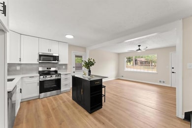 Kitchen featuring stainless steel appliances, white cabinetry, light wood finished floors, light countertops, and decorative backsplash