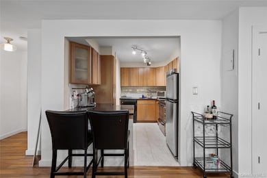 Kitchen with decorative backsplash, appliances with stainless steel finishes, glass insert cabinets, light wood-type flooring, and brown cabinets