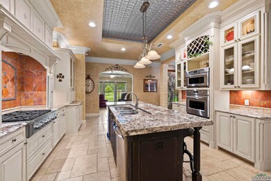 Kitchen featuring stone tile flooring, ornamental molding, a raised ceiling, appliances with stainless steel finishes, and an island with sink