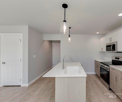 Kitchen with stainless steel appliances, light wood-style floors, hanging light fixtures, recessed lighting, and white cabinets