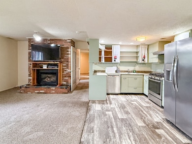 Basement kitchen featuring appliances with stainless steel finishes, light countertops, a textured ceiling, open shelves, and open floor plan
