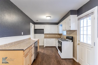 Kitchen featuring gas range, dark wood-style floors, light countertops, white cabinets, and a textured wall