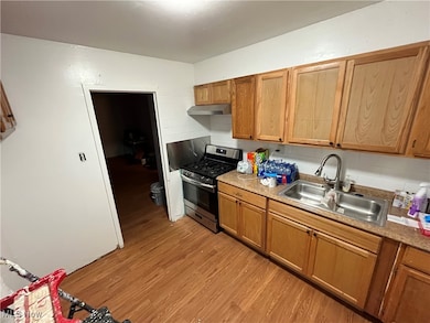 Kitchen with tasteful backsplash, stainless steel range with gas stovetop, light wood finished floors, brown cabinetry, and under cabinet range hood