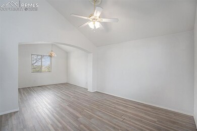 Unfurnished room with wood finished floors, vaulted ceiling, a ceiling fan, arched walkways, and baseboards