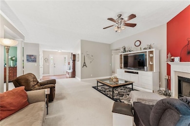 Living area with ceiling fan, a fireplace, and light carpet