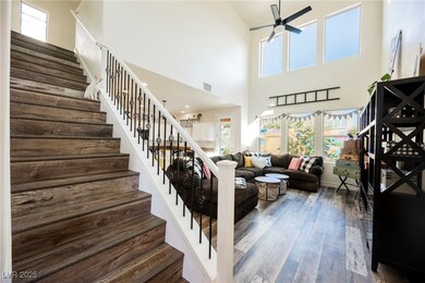 Living room with stairs, healthy amount of natural light, wood-style floors, a high ceiling, and ceiling fan