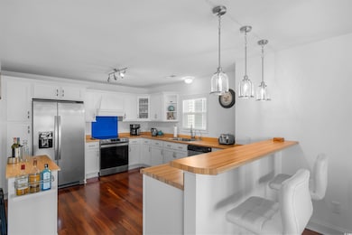 Kitchen featuring a peninsula, appliances with stainless steel finishes, white cabinets, hanging light fixtures, and wooden counters