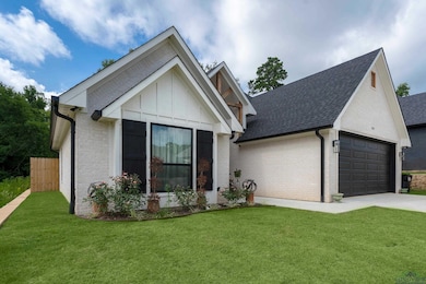 Ranch-style home featuring an attached garage, concrete driveway, brick siding, and roof with shingles