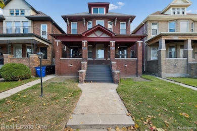 American foursquare style home featuring brick siding, a front lawn, stairway, and a porch