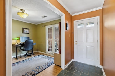 Foyer featuring baseboards, a textured ceiling, visible vents, and crown molding