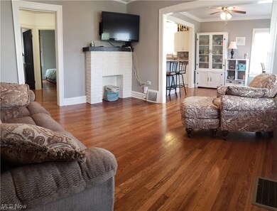 Living room featuring ornamental molding, dark hardwood / wood-style floors, ceiling fan, and a brick fireplace