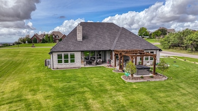 Back elevation showing large back porch living area, double pergolas, spa and grilling area. 3 entries into home from back porch- Owner's suite, kitchen area and access to half bath. Sodded and irrigated lot with large stone retaining wall on garage side.