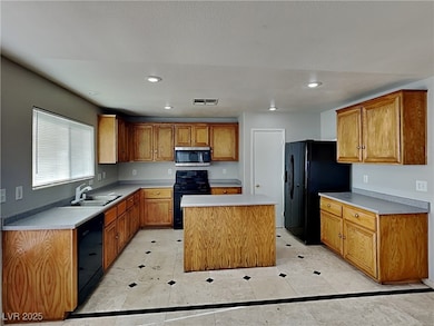 Kitchen featuring brown cabinetry, black appliances, light countertops, recessed lighting, and a center island