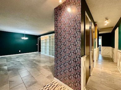 Hall with a textured ceiling, a chandelier, and a wainscoted wall