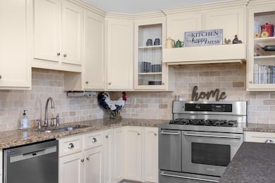 Kitchen with appliances with stainless steel finishes, a sink, decorative backsplash, light stone countertops, and glass insert cabinets