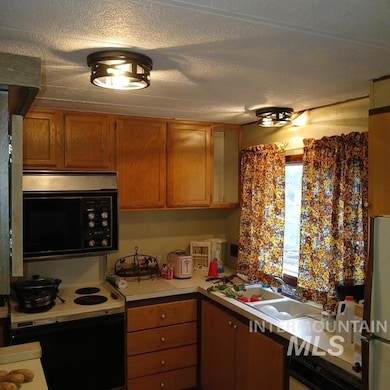Kitchen featuring brown cabinetry, black appliances, light countertops, and a textured ceiling
