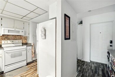 Kitchen with white appliances, wood finished floors, and white cabinets