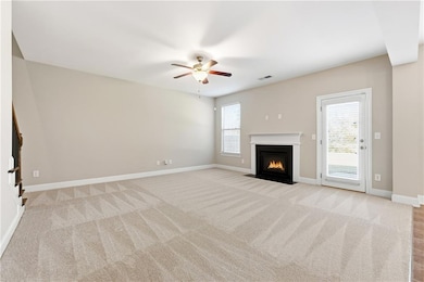 Unfurnished living room with light colored carpet, a fireplace with flush hearth, plenty of natural light, and a ceiling fan