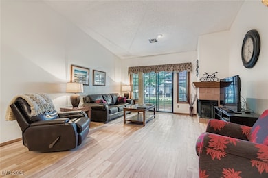 Living area with a tiled fireplace, a textured ceiling, and light wood finished floors