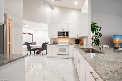 Kitchen with white electric range oven, a sink, stainless steel microwave, a towering ceiling, and light stone countertops