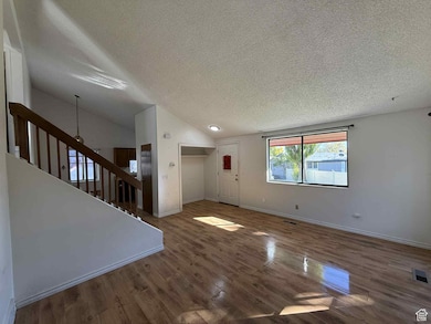 Unfurnished living room featuring vaulted ceiling, a textured ceiling, and wood finished floors