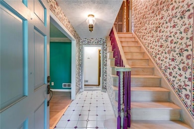 Foyer entrance with stairs, wallpapered walls, and a textured ceiling