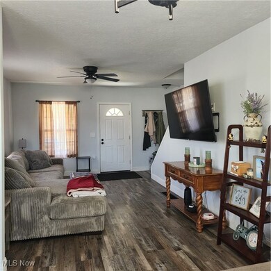 Living room with a textured ceiling, dark wood-style flooring, and a ceiling fan