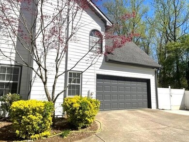 View of side of home with roof with shingles, driveway, and a gate