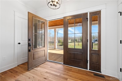 Foyer with visible vents, baseboards, ornamental molding, light wood-type flooring, and an inviting chandelier