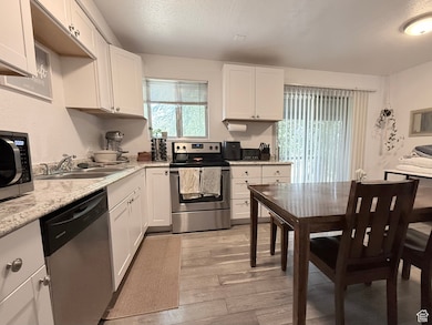 Kitchen with appliances with stainless steel finishes, light countertops, white cabinetry, light wood-style floors, and a textured ceiling