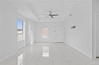 Tiled empty room with ceiling fan, a tray ceiling, and crown molding