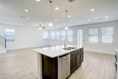 Kitchen with open floor plan, light wood finished floors, decorative light fixtures, dishwasher, and a center island with sink