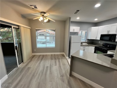 Kitchen featuring black appliances, white cabinets, light stone countertops, light wood-type flooring, and recessed lighting