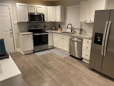 Kitchen with tasteful backsplash, white cabinetry, light hardwood / wood-style floors, sink, and stainless steel appliances