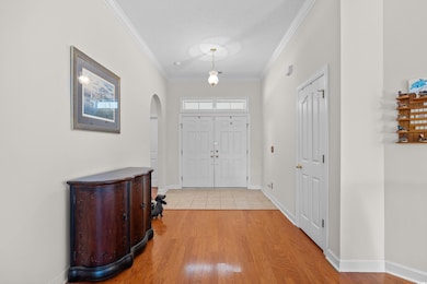 Foyer with arched walkways, ornamental molding, light wood-type flooring, and baseboards