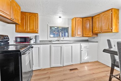 Kitchen with black range with electric stovetop, a textured ceiling, light wood-type flooring, brown cabinetry, and dark countertops