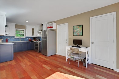 Kitchen with appliances with stainless steel finishes, white cabinets, tasteful backsplash, blue cabinets, and light wood-type flooring