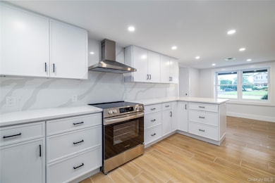 Kitchen featuring stainless steel range with electric stovetop, white cabinets, wall chimney range hood, and recessed lighting