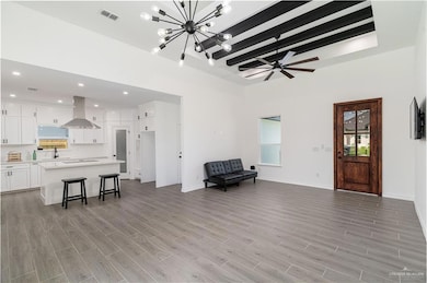 Living room featuring beam ceiling, light wood-style floors, a chandelier, baseboards, and a towering ceiling